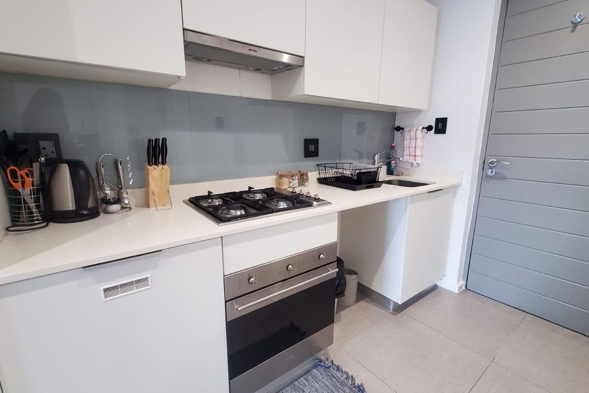 Modern kitchen featuring white cabinetry, stone countertops, a gas hob, built-in oven, and a sleek glass splashback.