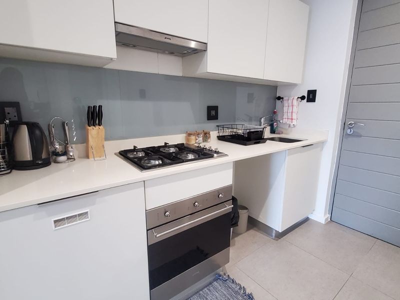 Modern kitchen featuring white cabinetry, stone countertops, a gas hob, built-in oven, and a sleek glass splashback.
