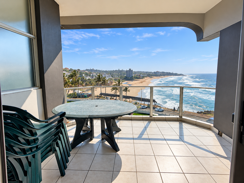 Spacious covered balcony featuring tiled flooring and a glass balustrade, offering panoramic ocean and coastal views.
