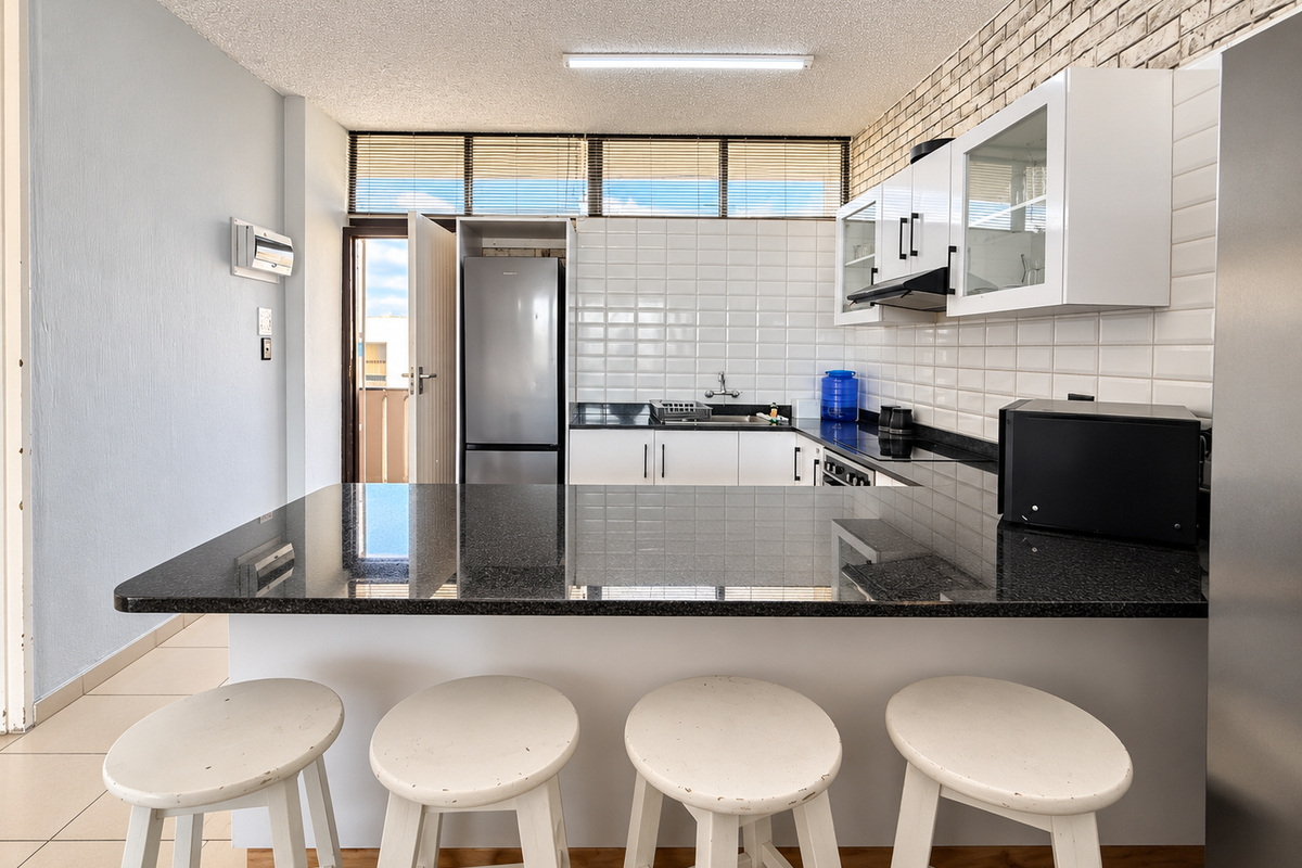 Modern kitchen featuring a granite breakfast bar, subway tile backsplash, and an exposed brick feature wall, offering a functional and stylish cooking space.