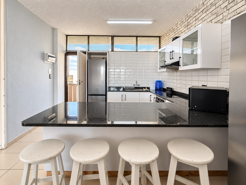 Modern kitchen featuring a granite breakfast bar, subway tile backsplash, and an exposed brick feature wall, offering a functional and stylish cooking space.