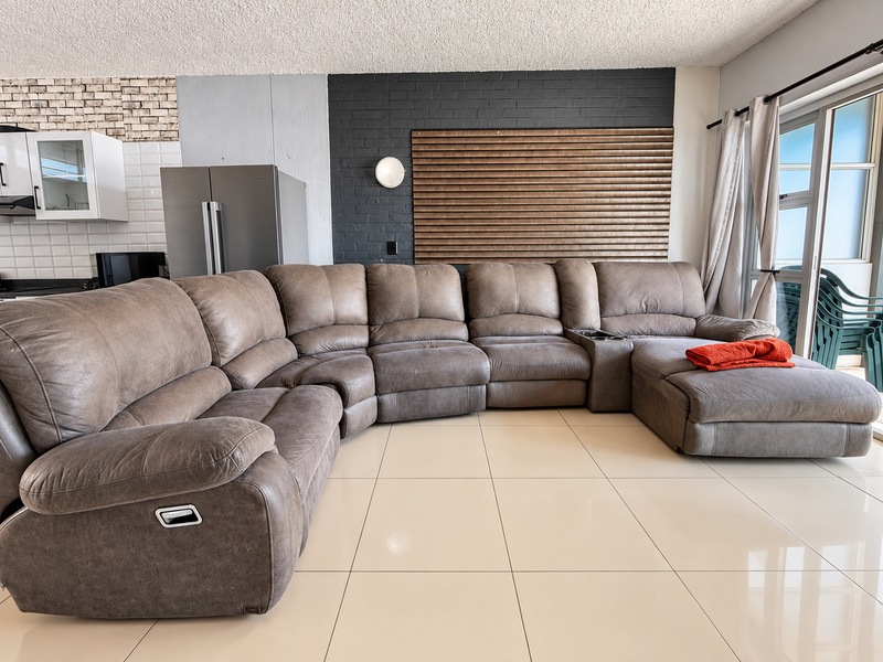 Open-plan living area featuring large format floor tiles, a dark brick feature wall, and direct access to an outdoor balcony through sliding glass doors.