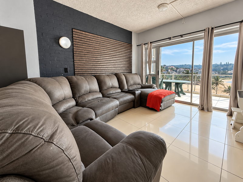A bright living room featuring large sliding glass doors that open to a balcony with coastal views, complemented by a dark brick feature wall.