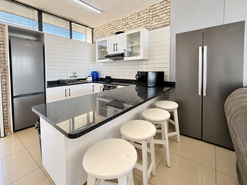 Modern kitchen featuring granite countertops, subway tile backsplash, exposed brick wall, and ample built-in cabinetry with a breakfast bar area.