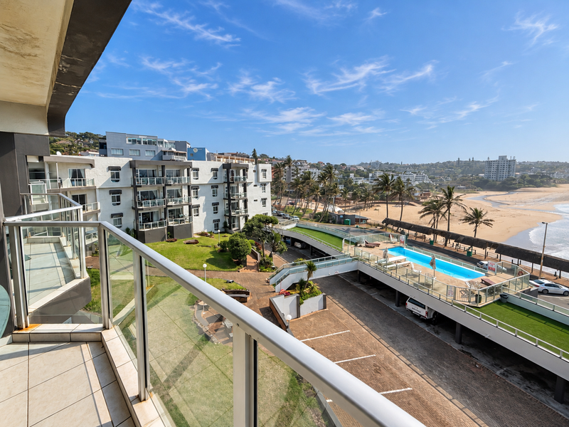 Spacious balcony overlooking the apartment complex grounds, swimming pool, and coastal beach view.