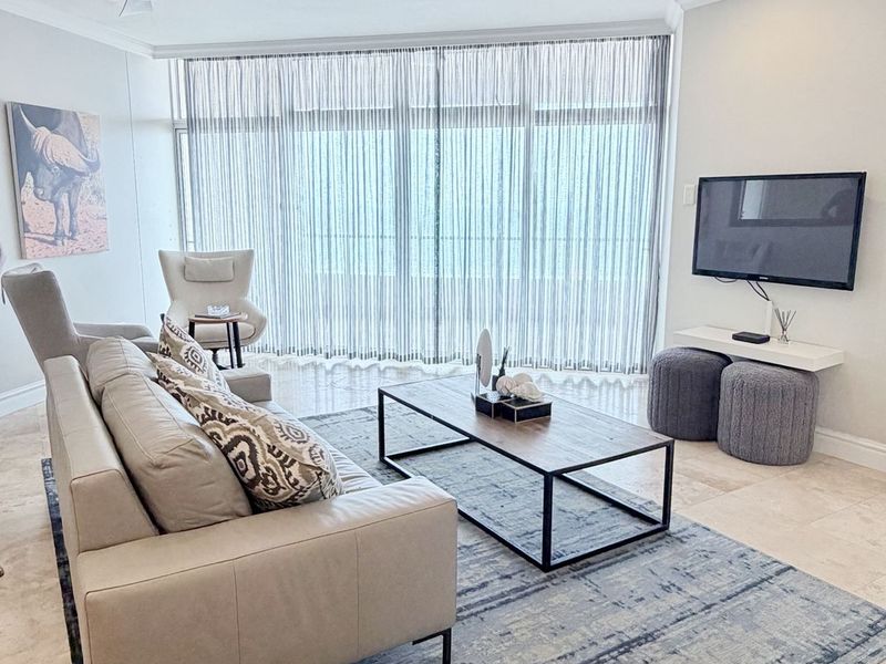 A bright and modern living room featuring tiled flooring, dual ceiling fans, recessed lighting, and large floor-to-ceiling windows with sheer curtains.