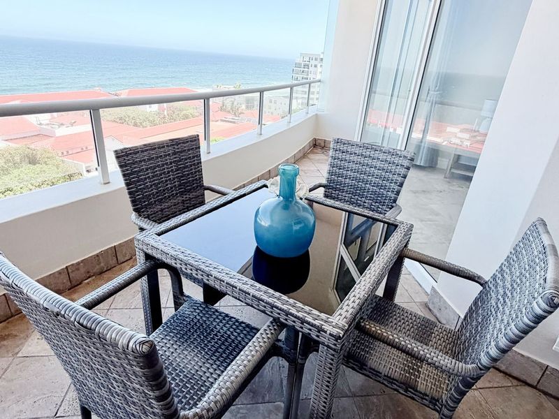 A spacious balcony featuring tiled flooring, a glass balustrade, and expansive sliding doors, offering panoramic ocean views.