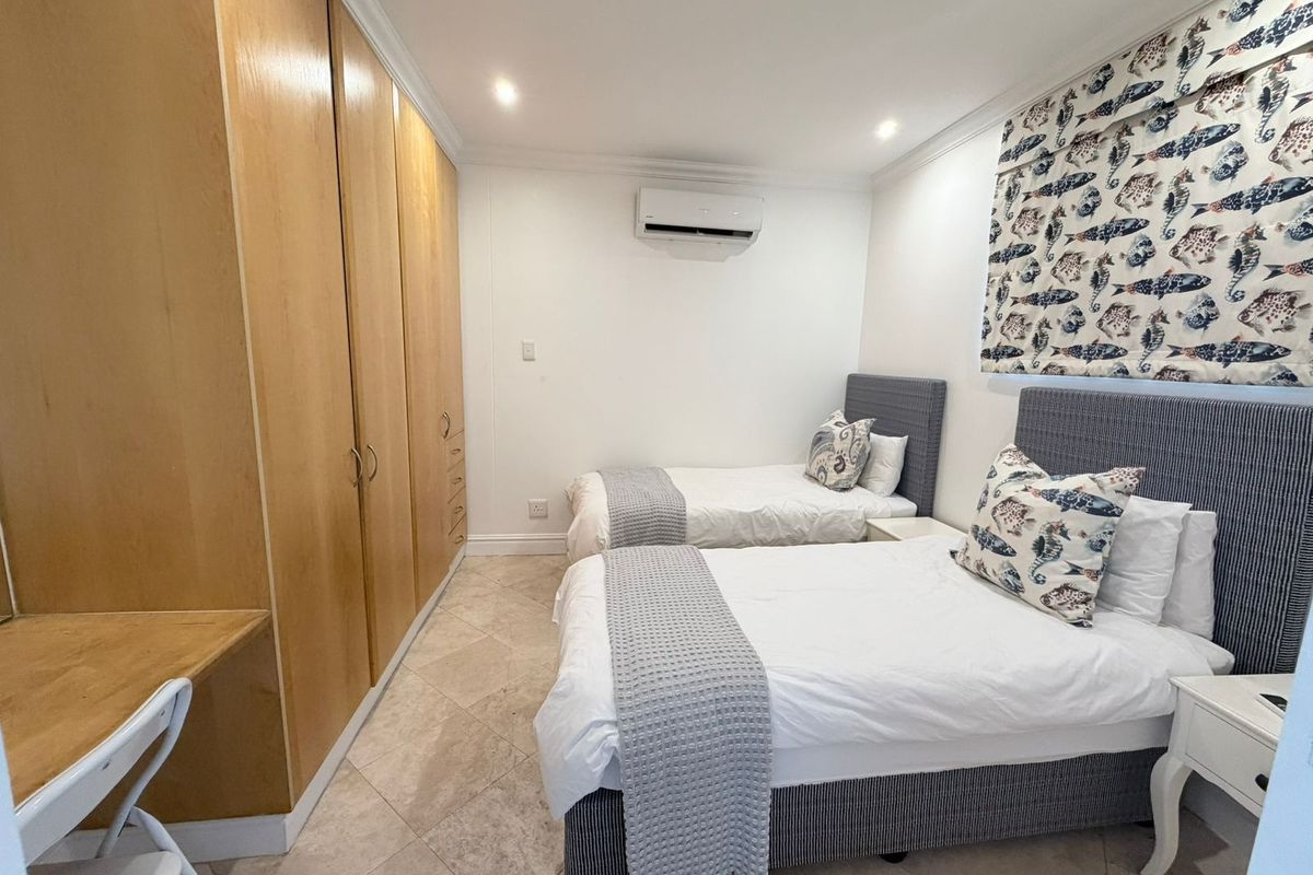 A well-maintained bedroom featuring built-in wooden cupboards, a built-in desk, tiled flooring, and a wall-mounted split-system air conditioner.