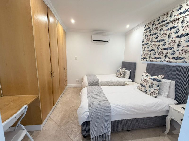 A well-maintained bedroom featuring built-in wooden cupboards, a built-in desk, tiled flooring, and a wall-mounted split-system air conditioner.
