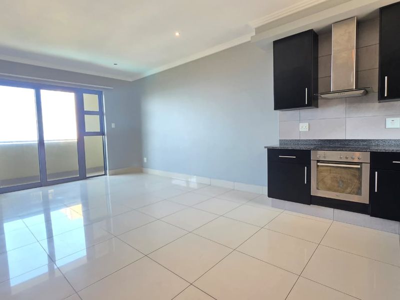 Modern open-plan living area featuring a sleek kitchen with dark cabinetry, granite countertops, stainless steel appliances, and large sliding doors leading to a balcony.