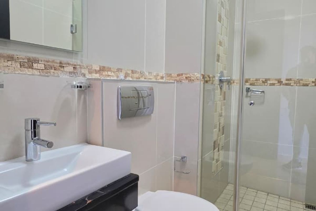 Modern bathroom featuring a glass-enclosed shower, wall-mounted toilet with chrome flush plate, and a vanity basin with storage.