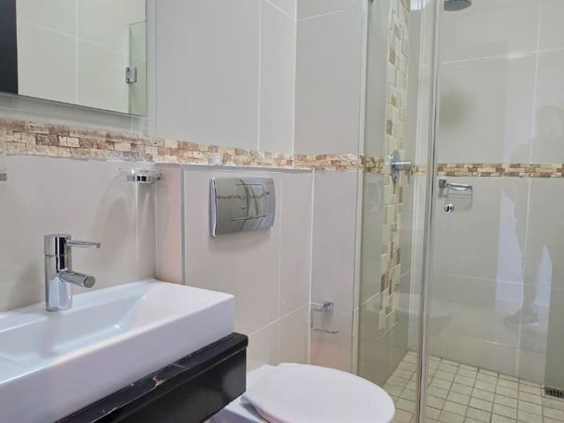 Modern bathroom featuring a glass-enclosed shower, wall-mounted toilet with chrome flush plate, and a vanity basin with storage.