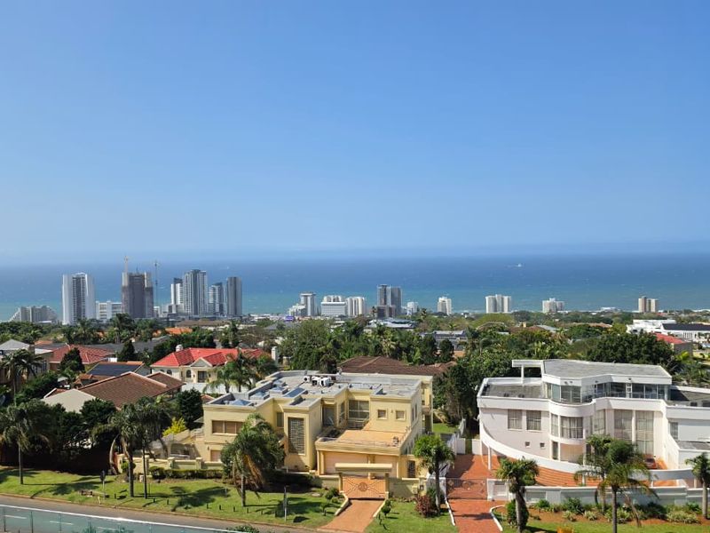 Elevated panoramic view overlooking the coastal cityscape and ocean, captured from an apartment balcony.