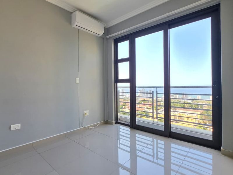 A bright, empty bedroom featuring tiled floors, a built-in cupboard, air conditioning, and a sliding door leading to a balcony with scenic views.