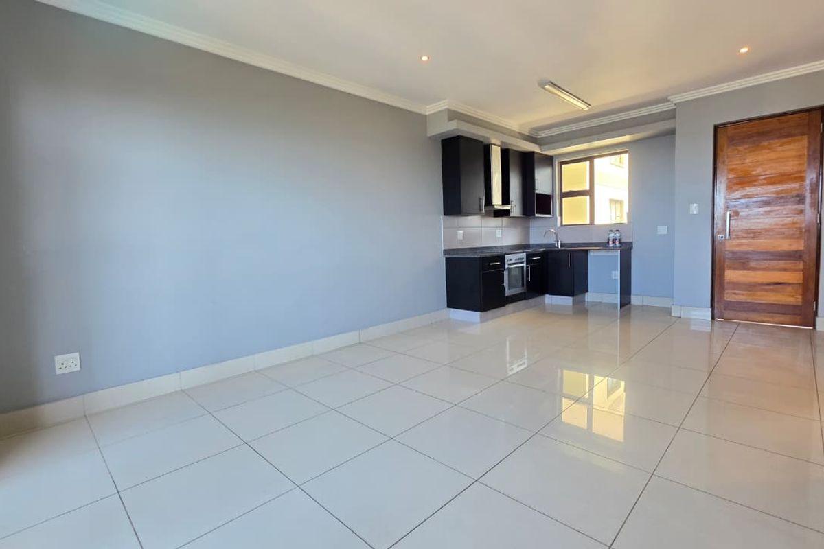 An open-plan living area featuring tiled flooring and a compact kitchen with built-in cabinetry, oven, and extractor fan.