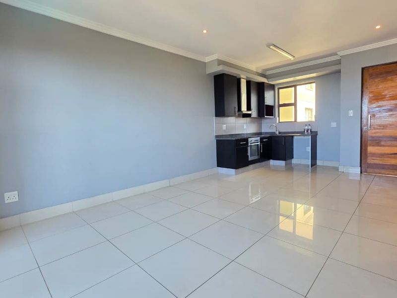 An open-plan living area featuring tiled flooring and a compact kitchen with built-in cabinetry, oven, and extractor fan.