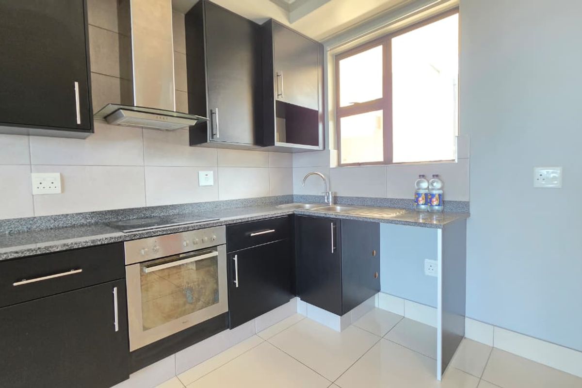 Modern kitchen featuring dark cabinetry, granite countertops, built-in oven, hob, extractor fan, and tiled flooring with a functional layout.