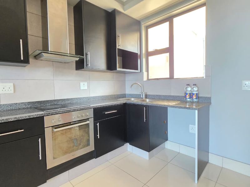 Modern kitchen featuring dark cabinetry, granite countertops, built-in oven, hob, extractor fan, and tiled flooring with a functional layout.
