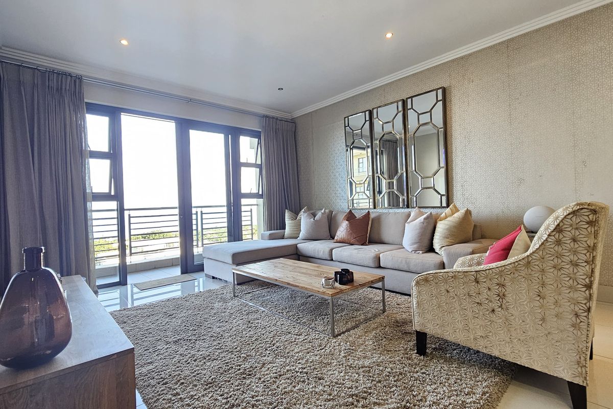 A well-maintained living room featuring tiled floors, textured wallpaper, recessed lighting, and large sliding glass doors providing access to the balcony.