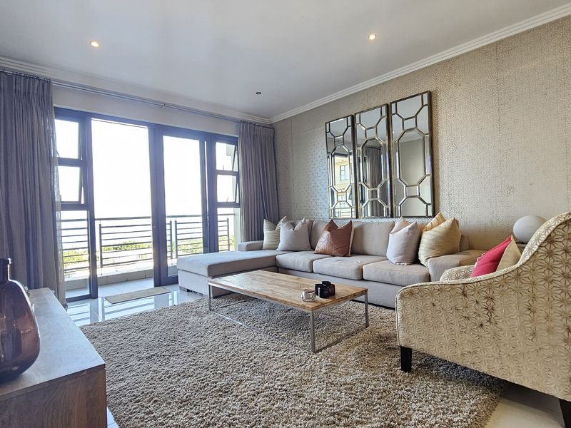 A well-maintained living room featuring tiled floors, textured wallpaper, recessed lighting, and large sliding glass doors providing access to the balcony.