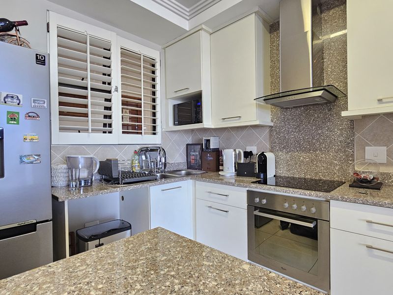 Modern kitchen featuring granite countertops, white cabinetry, stainless steel appliances including an oven and extractor fan, and plantation shutters for natural light control.