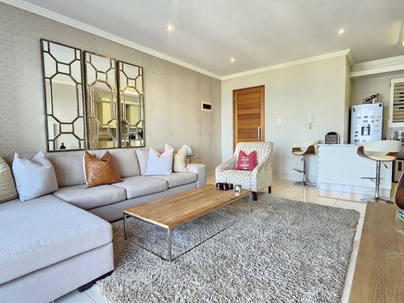An open-plan living area featuring tiled flooring, recessed lighting, and a breakfast bar connecting to the kitchen space.