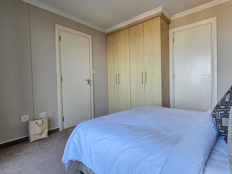 A well-maintained bedroom featuring neutral wall tones, carpeted flooring, and ample built-in wardrobe storage.