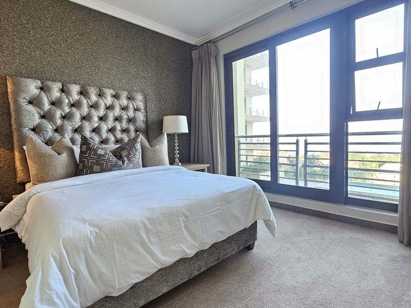 A well-maintained bedroom featuring a textured accent wall, neutral carpeting, and large sliding glass doors providing access to a private balcony.