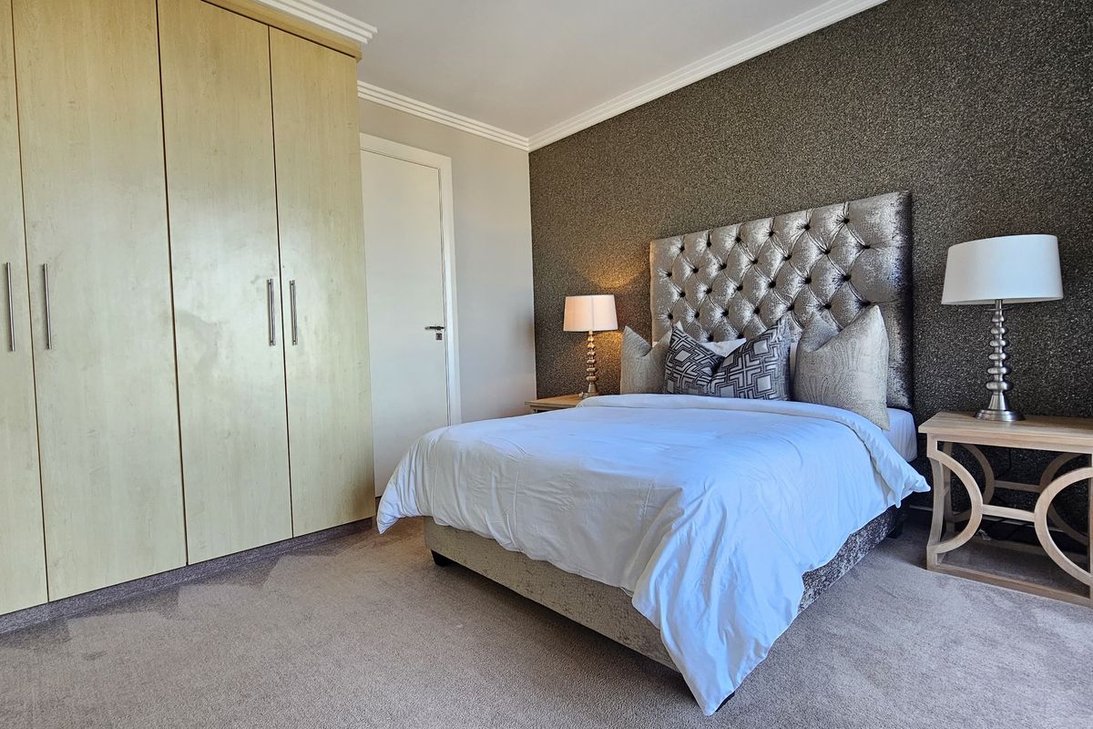 A well-maintained bedroom featuring a built-in wardrobe, neutral carpet flooring, and a decorative textured feature wall.