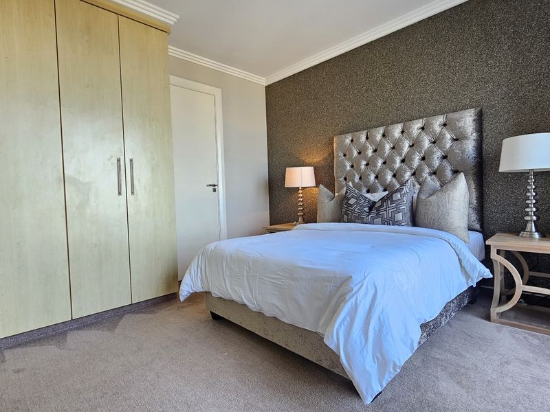 A well-maintained bedroom featuring a built-in wardrobe, neutral carpet flooring, and a decorative textured feature wall.