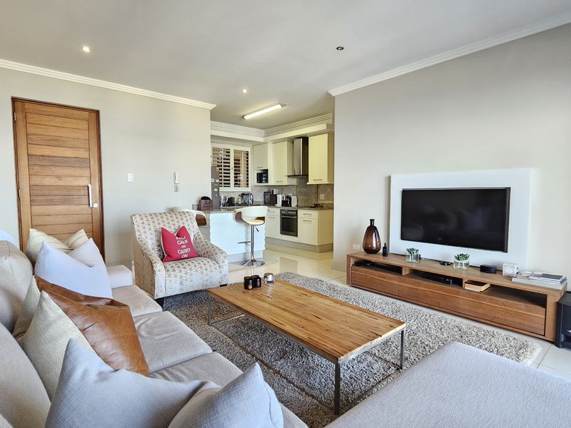 Spacious open-plan living area featuring a modern kitchen with stone countertops, integrated appliances, and tiled flooring, seamlessly flowing into the lounge space.