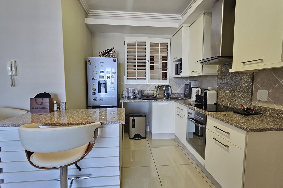 Modern kitchen featuring granite countertops, built-in oven, electric hob, extractor fan, and a breakfast bar with tiled flooring.