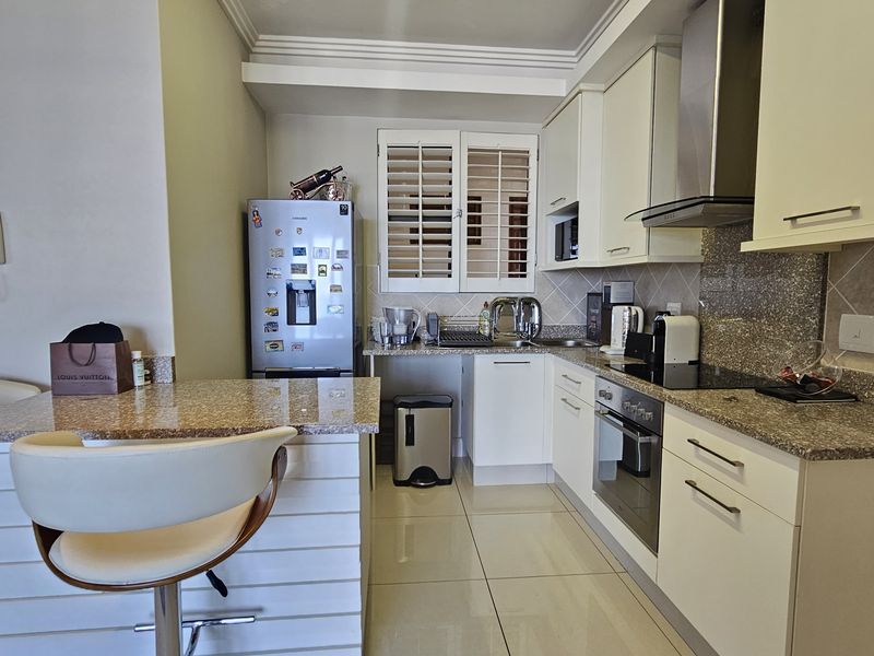 Modern kitchen featuring granite countertops, built-in oven, electric hob, extractor fan, and a breakfast bar with tiled flooring.