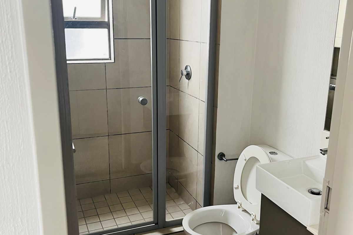 A functional bathroom featuring a glass-enclosed shower, a wall-mounted vanity, and neutral floor and wall tiling.