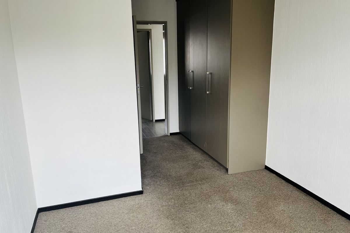 A vacant bedroom featuring neutral wall finishes, carpeted flooring, and built-in cupboards, providing a clean and functional space.