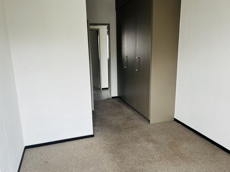 A vacant bedroom featuring neutral wall finishes, carpeted flooring, and built-in cupboards, providing a clean and functional space.