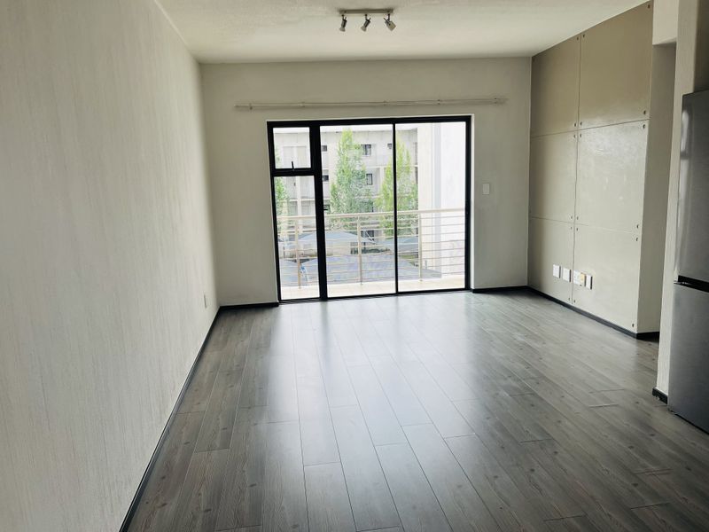 An open-plan living area featuring modern laminate flooring, built-in cabinetry, and a sliding glass door leading to a balcony.