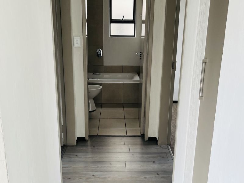 A clean, well-maintained hallway featuring modern laminate flooring and access to adjacent rooms, including a bathroom with tiled finishes.