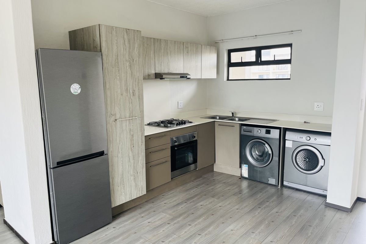Modern kitchen featuring light wood-look cabinetry, gas hob, built-in oven, extractor fan, and integrated space for laundry appliances.