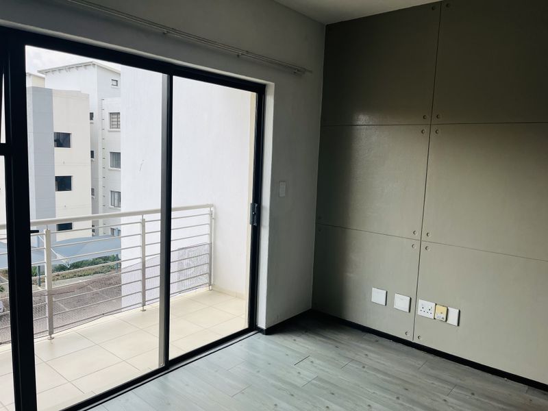 An empty living room featuring modern laminate flooring, a decorative feature wall, and large sliding glass doors providing access to a private balcony.