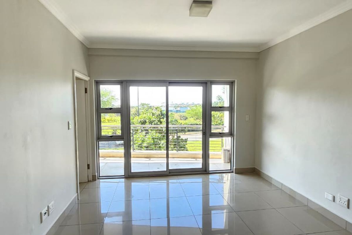 A bright, empty living room featuring neutral tiled flooring and a large sliding glass door that opens onto a balcony with outdoor views.