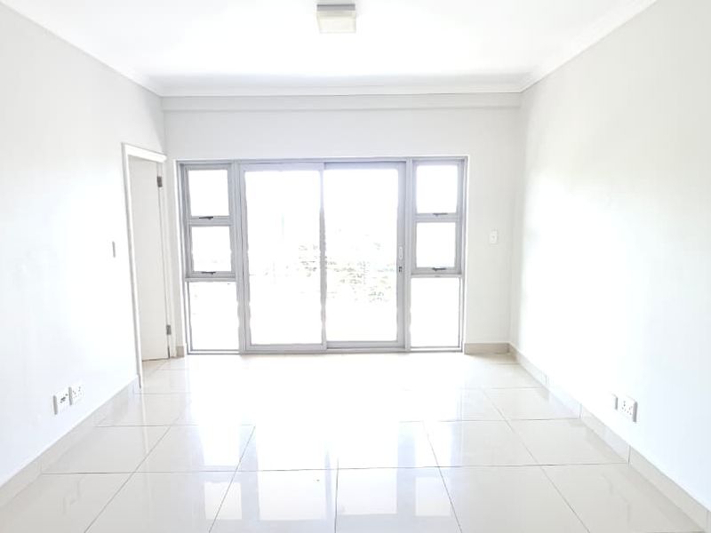 A bright, empty living room featuring neutral tiled flooring and a large sliding glass door providing natural light.