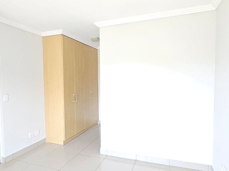 A bright, empty bedroom featuring neutral tiled flooring and ample built-in cupboard storage space.