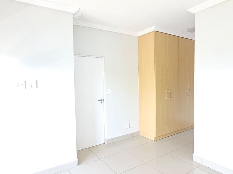 A bright, empty bedroom featuring neutral tiled flooring, built-in wooden cupboards, and clean white walls, offering a versatile space ready for personalization.