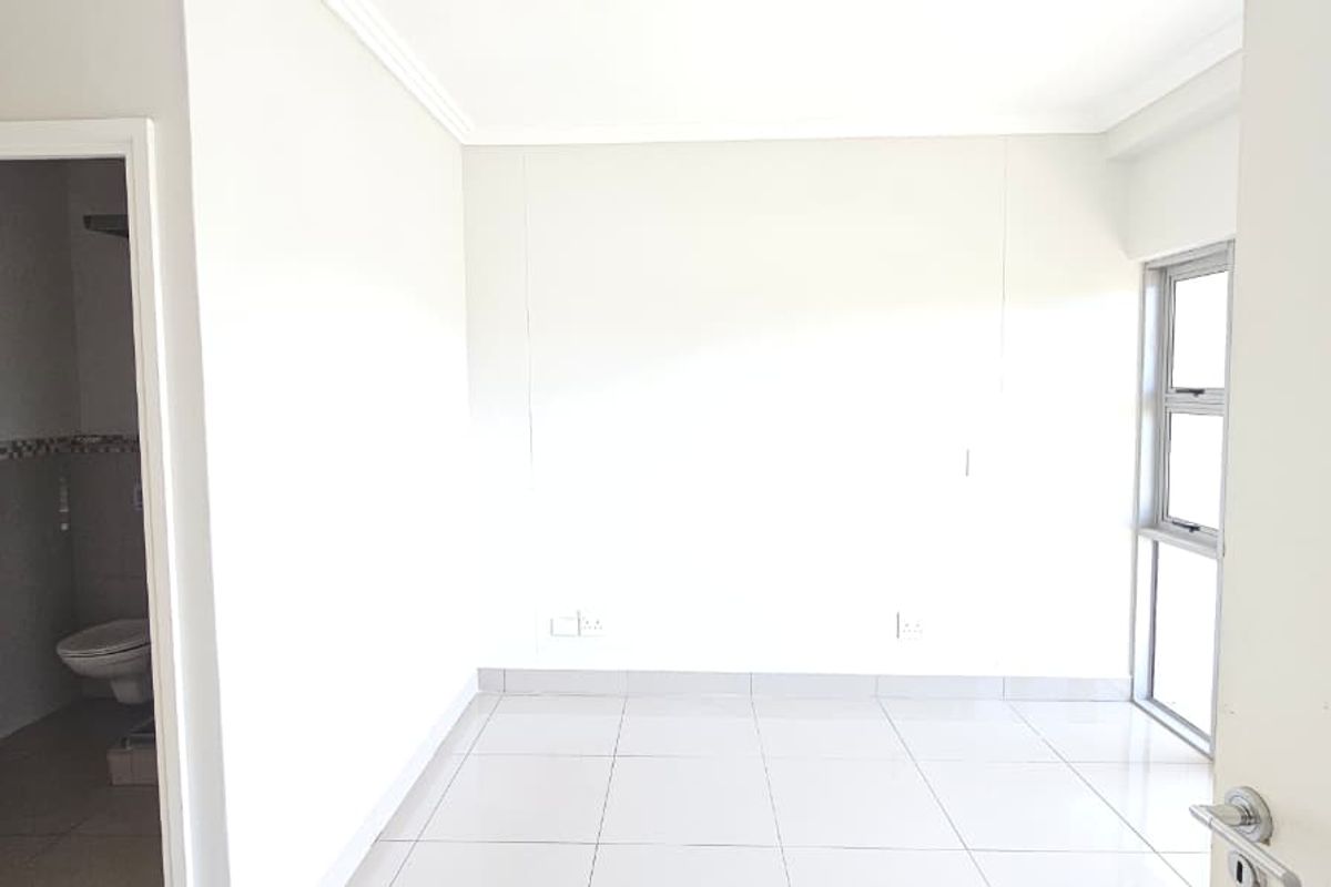 A bright, empty bedroom featuring neutral tiled flooring, clean white walls, and an en-suite bathroom access.