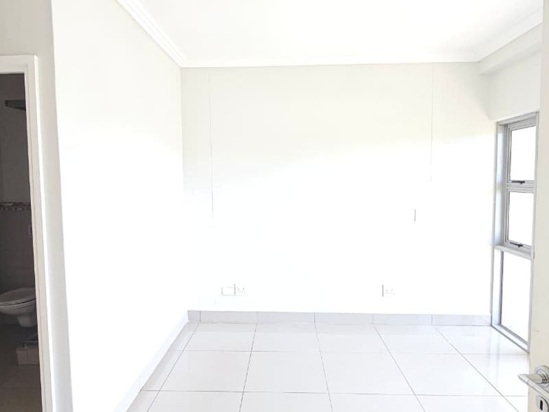 A bright, empty bedroom featuring neutral tiled flooring, clean white walls, and an en-suite bathroom access.