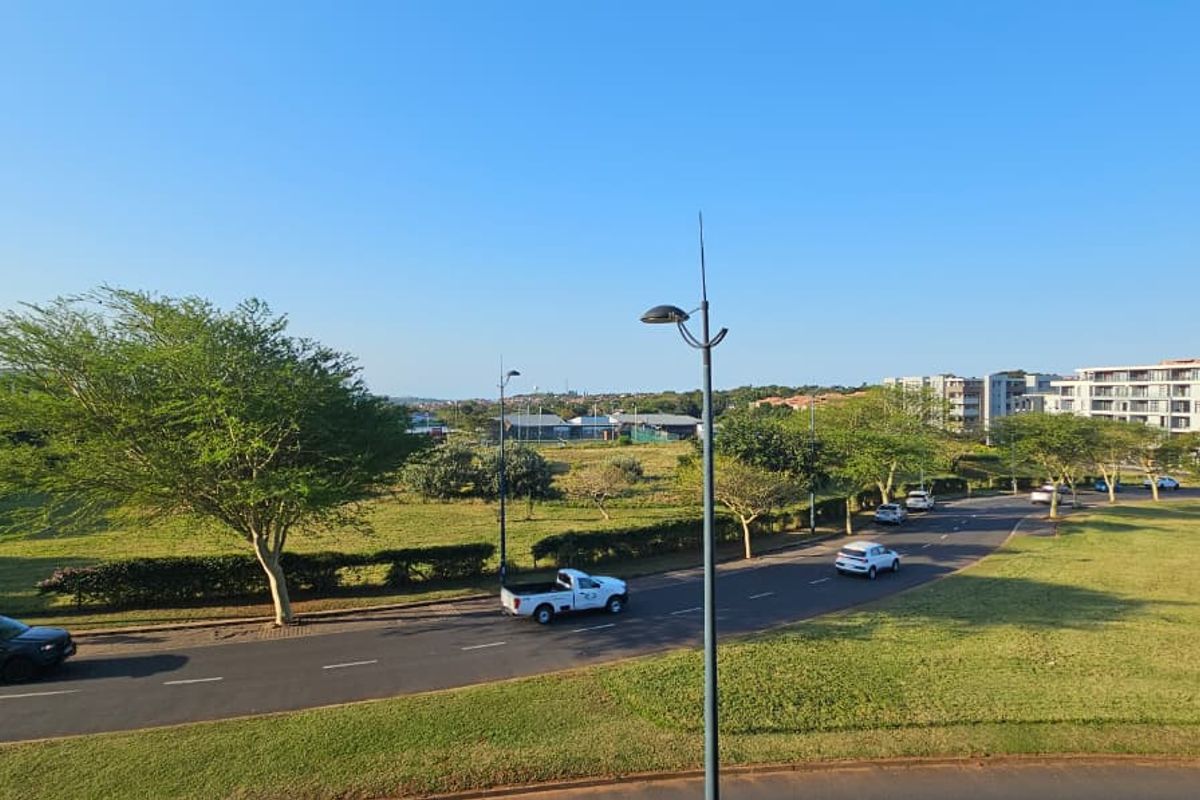 An elevated view overlooking a suburban street, green parkland, and surrounding apartment complexes under a clear blue sky.