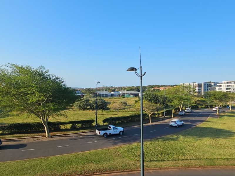 An elevated view overlooking a suburban street, green parkland, and surrounding apartment complexes under a clear blue sky.