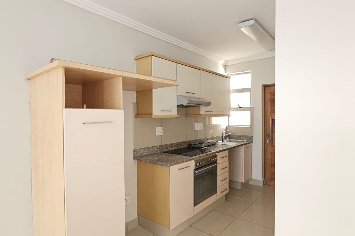 A functional kitchen featuring light-toned cabinetry, granite countertops, a built-in oven with hob, and tiled flooring.