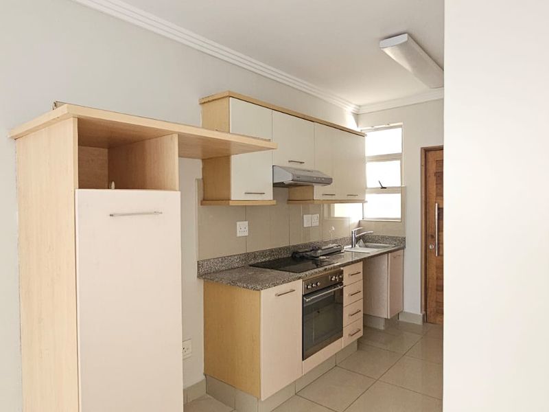 A functional kitchen featuring light-toned cabinetry, granite countertops, a built-in oven with hob, and tiled flooring.